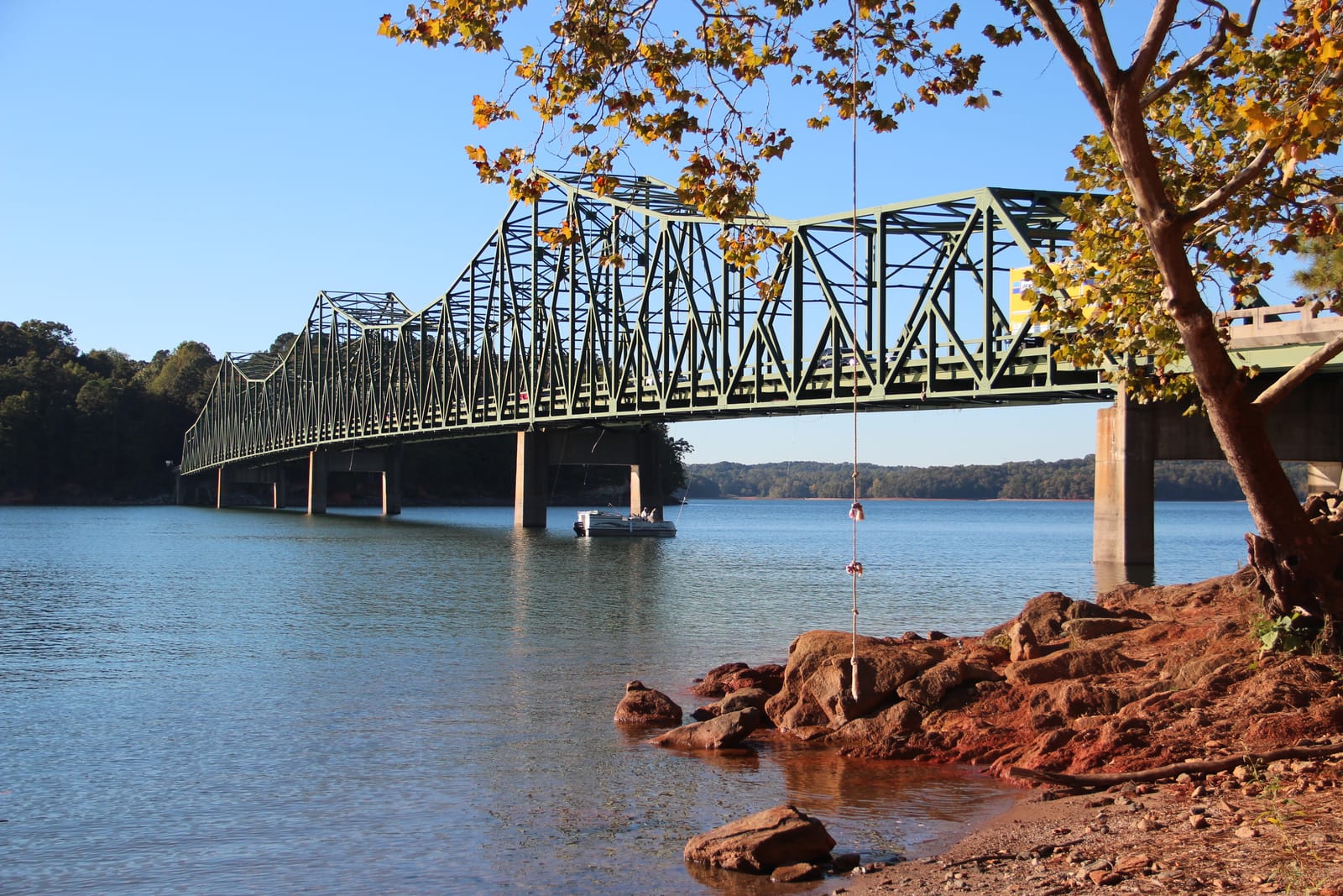 Browns Bridge, a green steel truss bridge across Lake Lanier, with red clay boulders exposed at the waterline in October
