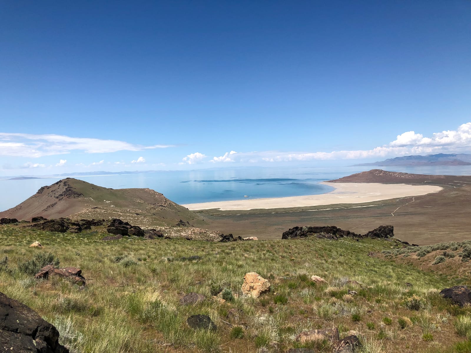 White Rock Bay on Antelope Island: a pale curved beach and blue water beyond green, grassy hills