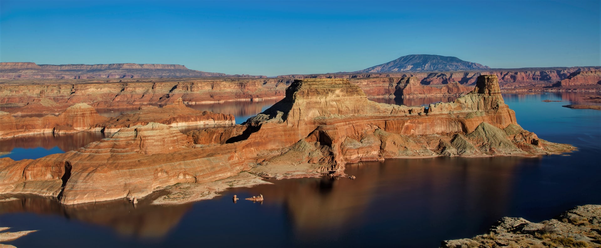 Gunsight Butte rising out of Lake Powell at sunset, red sandstone cliffs and deep blue water, Navajo Mountain on the horizon
